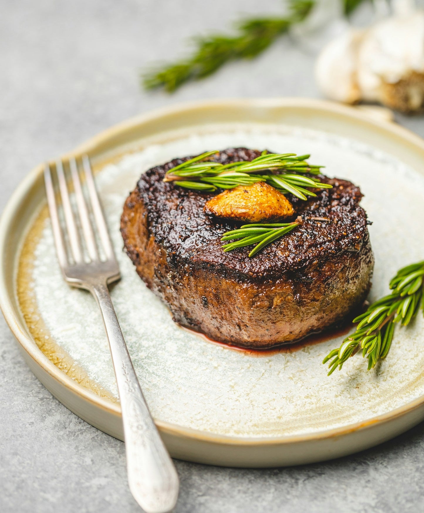 Reverse-seared beef steak topped with fresh rosemary and roasted garlic on a plate